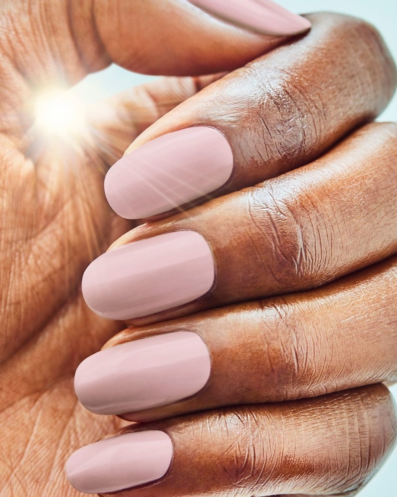Light pink rounded nails with the sun beaming through hand.