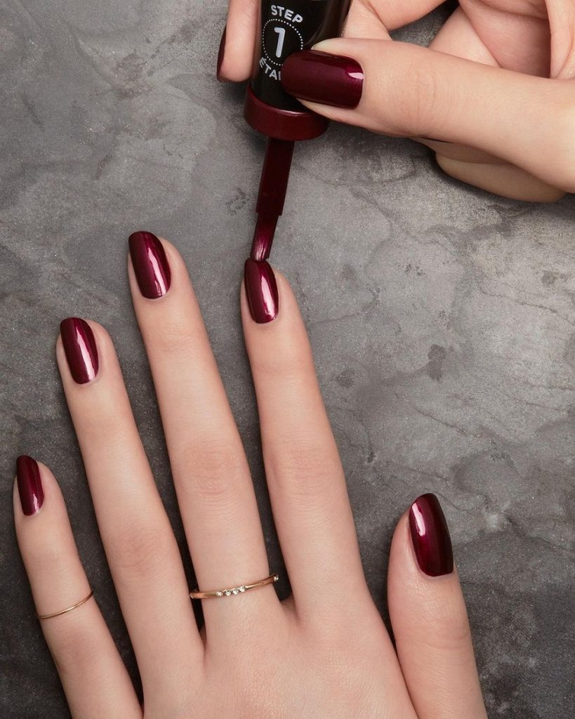 Woman applying red nail varnish to nails.