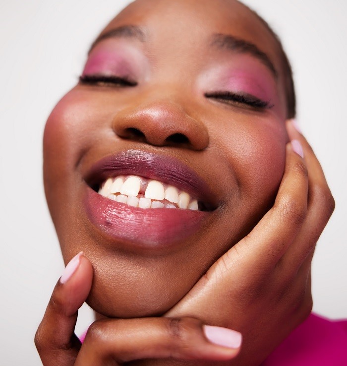 Model wearing pink makeup smiling with eyes closed.